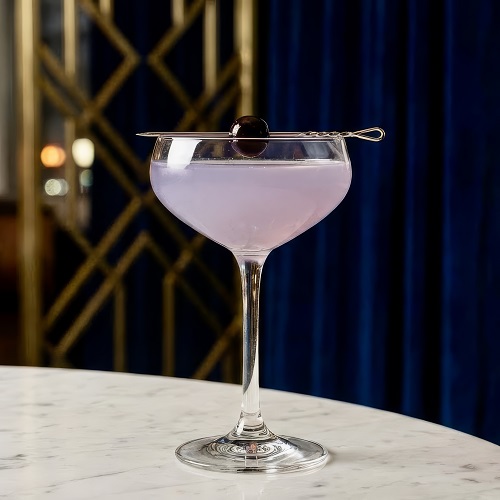 Lavender-hued Aviation cocktail in a coupe glass with cherry garnish.