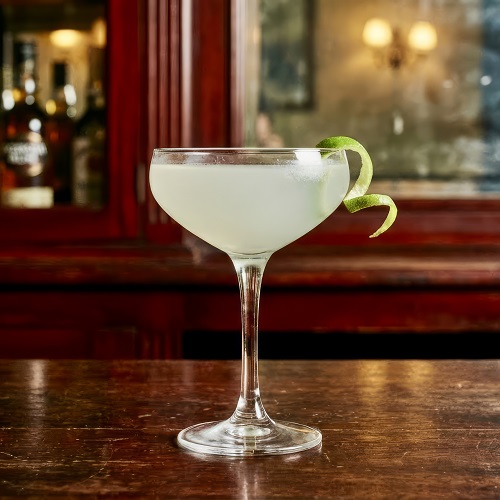 Classic Daiquiri cocktail in a chilled coupe glass with lime garnish, featuring rum, lime, and sugar mix.